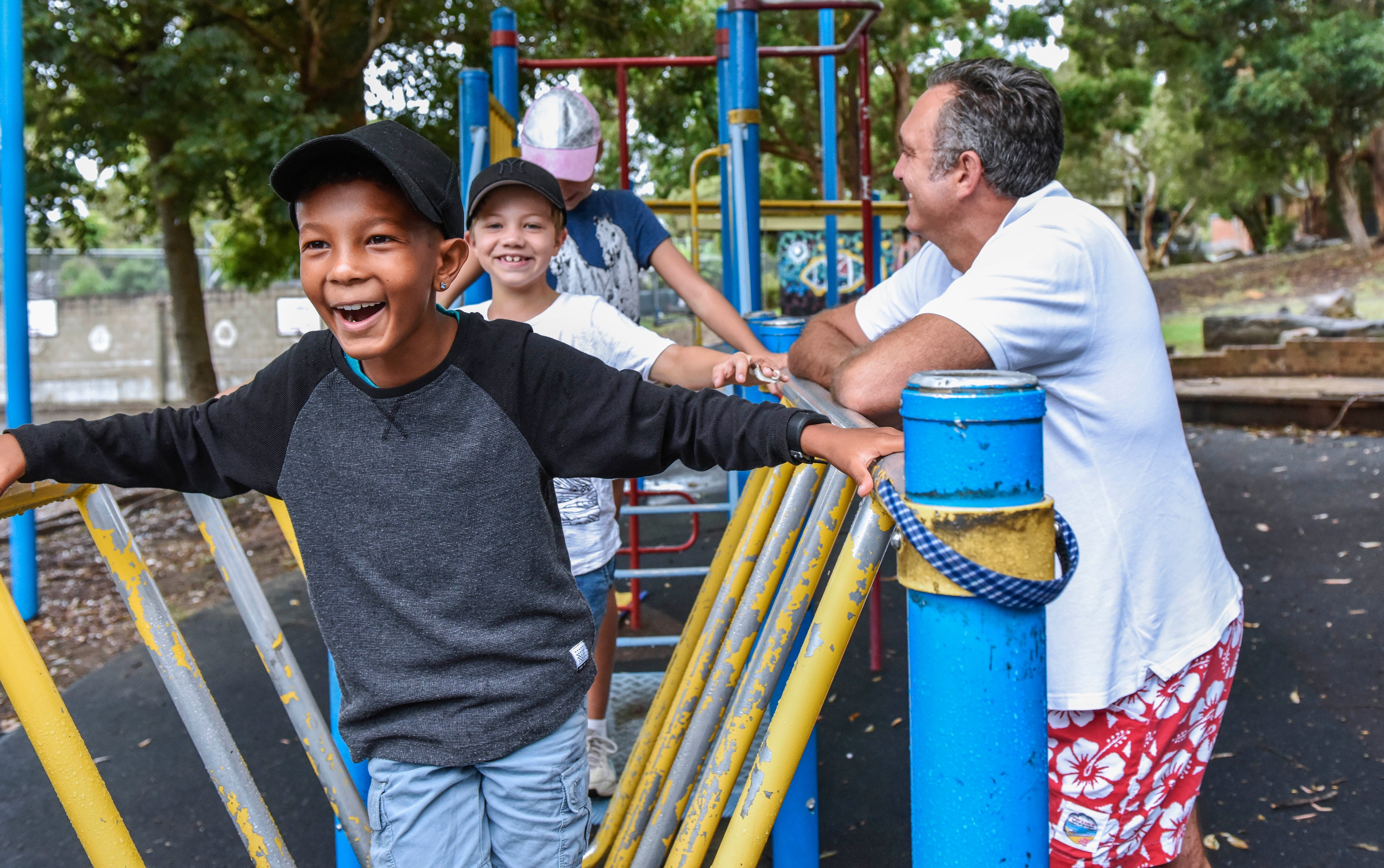 Two young boys on playground equipment supervised by male adult Two young boys on playground equipment supervised by male adult